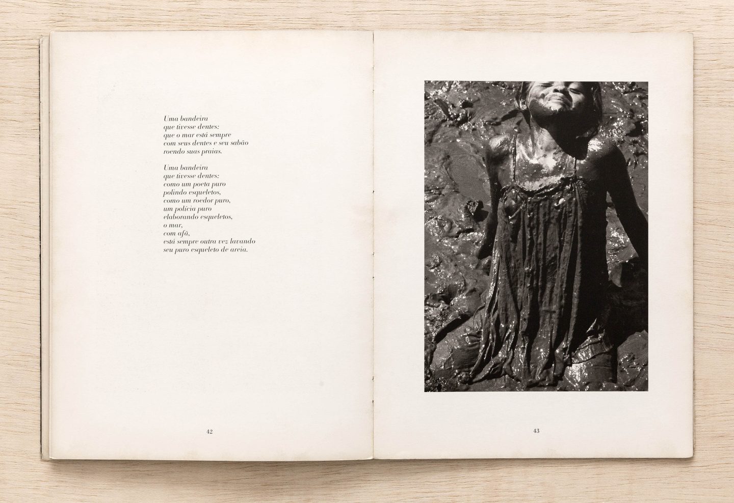 Livro aberto, na página esquerda um poema impresso e, na página direita, uma fotografia em preto e branco de uma menina tomando um banho de lama.